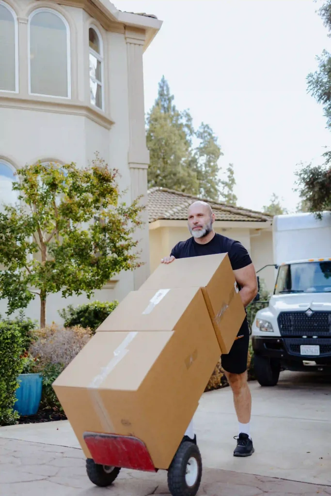 A strong Service Pro Movers team member using a hand truck to move large cardboard boxes outside a residential apartment complex in Sacramento