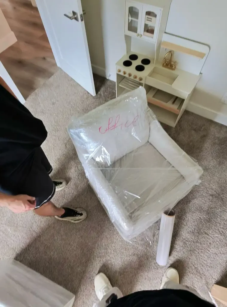 Movers securing wrapped furniture with straps inside a moving truck